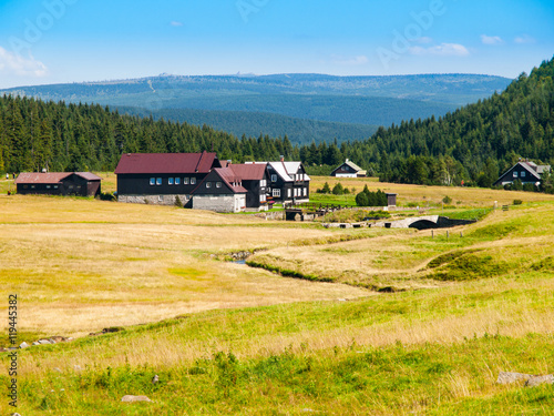 Large green meadows and rural mountain houses of Jizerka Village with Giant Mountains, or Krkonose, on the background, Jizera Mountains, Czech Republic.