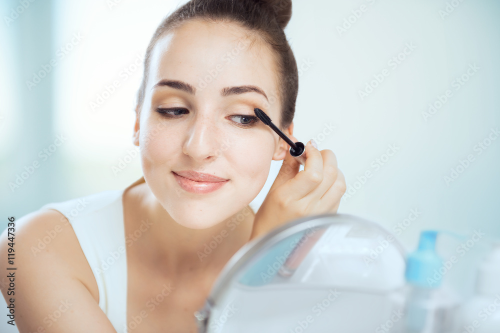 A young brunette woman putting on mascara, looking in the round A young brunette woman putting on mascara, looking in the round