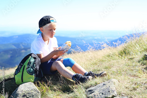 Wakacje w górach. 
Dziecko je kanapkę na górskim szlaku
