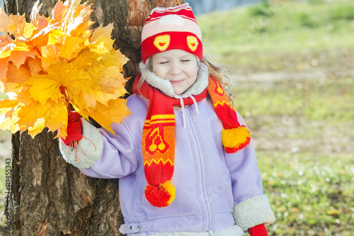 Smiling little girl holding yellow with orange autumn leaves bunch in hand outdoor portrait