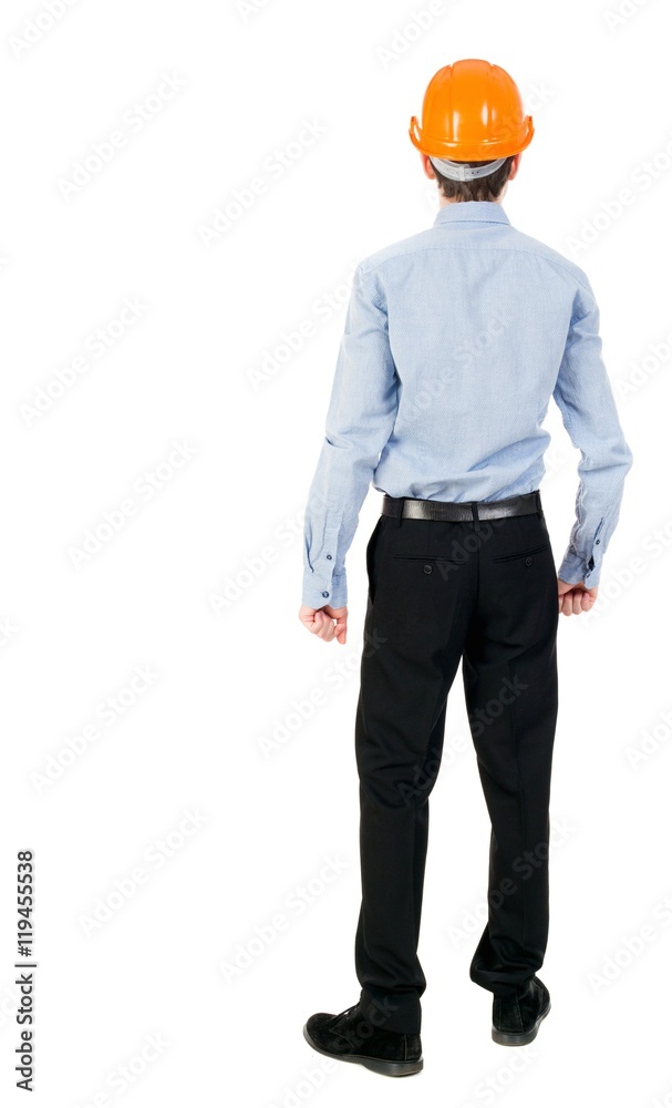 Backview of an engineer in construction helmet stands. Standing young guy. Curly businessman in a light jacket and a helmet sees something ahead. Backview of an engineer in construction helmet stands. Standing young guy. Curly businessman in a light jacket and a helmet sees something ahead.