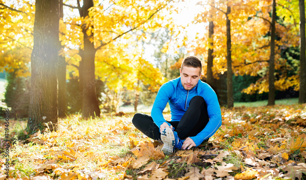 Runner sitting on the ground, tying shoelaces, autumn nature