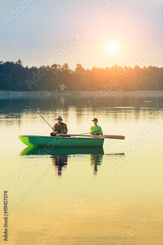 father and son catch fish from a boat at sunset