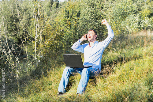 Happy man on nature with laptop and smartphone.