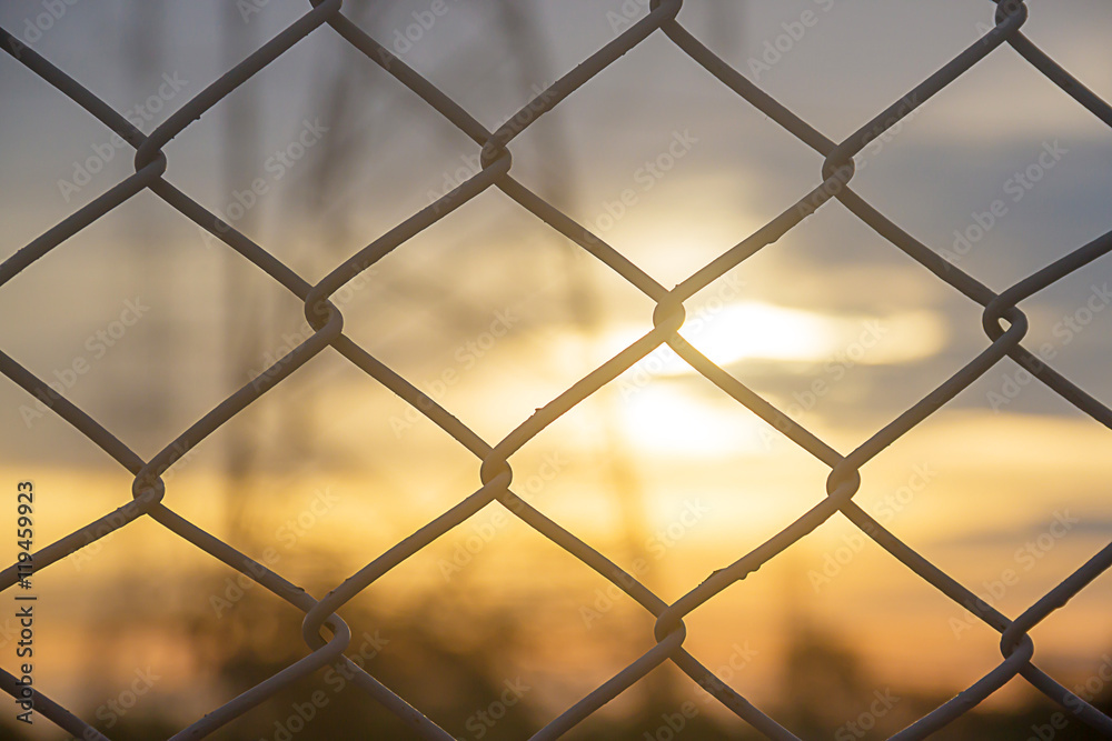 selected focus, mesh fence silhouetted against sunset sky with blurr Electricity pylon background selected focus, mesh fence silhouetted against sunset sky with blurr Electricity pylon background