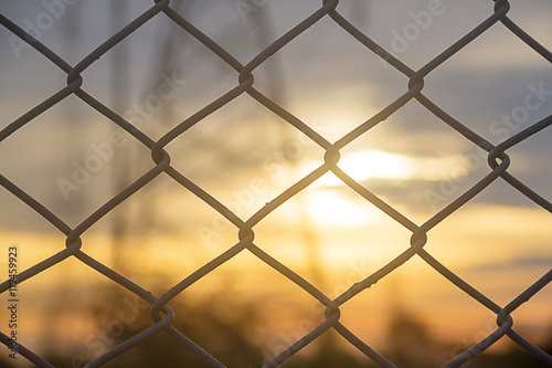 selected focus, mesh fence silhouetted against sunset sky with blurr Electricity pylon background