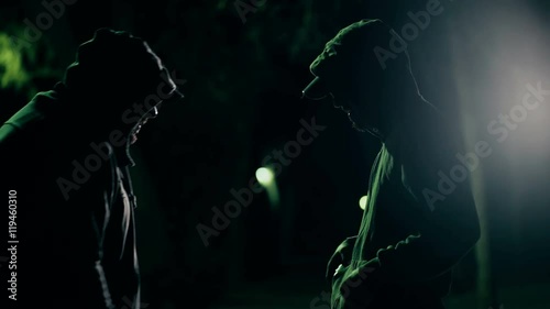 Two hooded criminals in dark park selling buying drugs