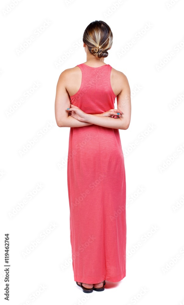 back view of standing young beautiful woman. A slender woman in a long red dress is standing with his hands behind his back. back view of standing young beautiful woman. A slender woman in a long red dress is standing with his hands behind his back.