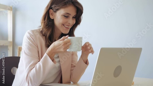 Happy business woman drinking coffee looking at computer display