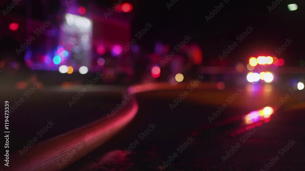 night time fire scene with fire hose and emergency vehicles
