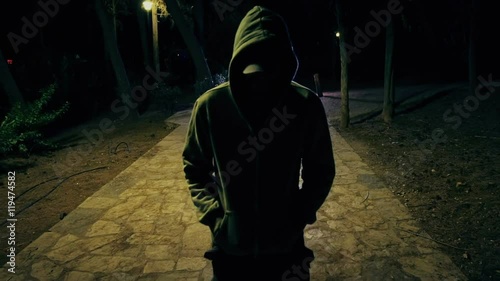 Suspicious hooded figure walks in a dark park at night,100p photo