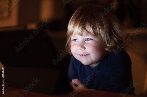 Obraz na plátne blonde two years old baby blue sweater, sitting inside home at night reading and