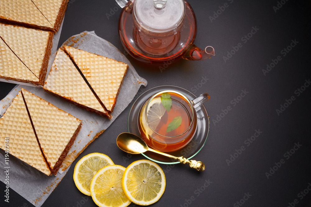 Sweet waffle triangular cakes with condensed milk and fresh hot black tea on a black table Sweet waffle triangular cakes with condensed milk and fresh hot black tea on a black table