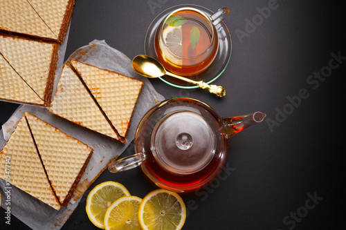 Sweet waffle triangular cakes with condensed milk and fresh hot black tea on a black table