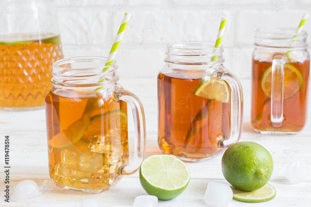 Iced tea in a glass jar with slice of lime. White wooden plank b Iced tea in a glass jar with slice of lime. White wooden plank b