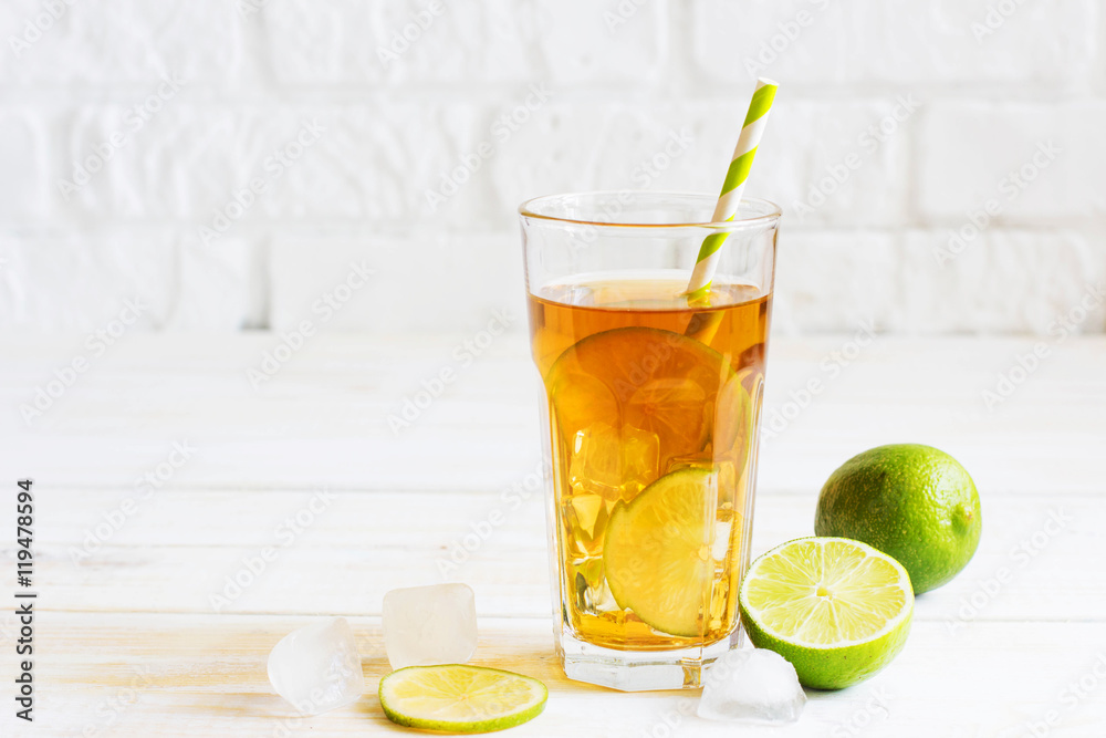 Fototapeta premium Ice tea in a glass with a slice of lime. White wooden plank back