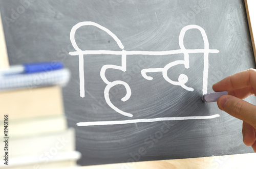Hand writing on a blackboard in a Hindi class. Some books and school materials.
