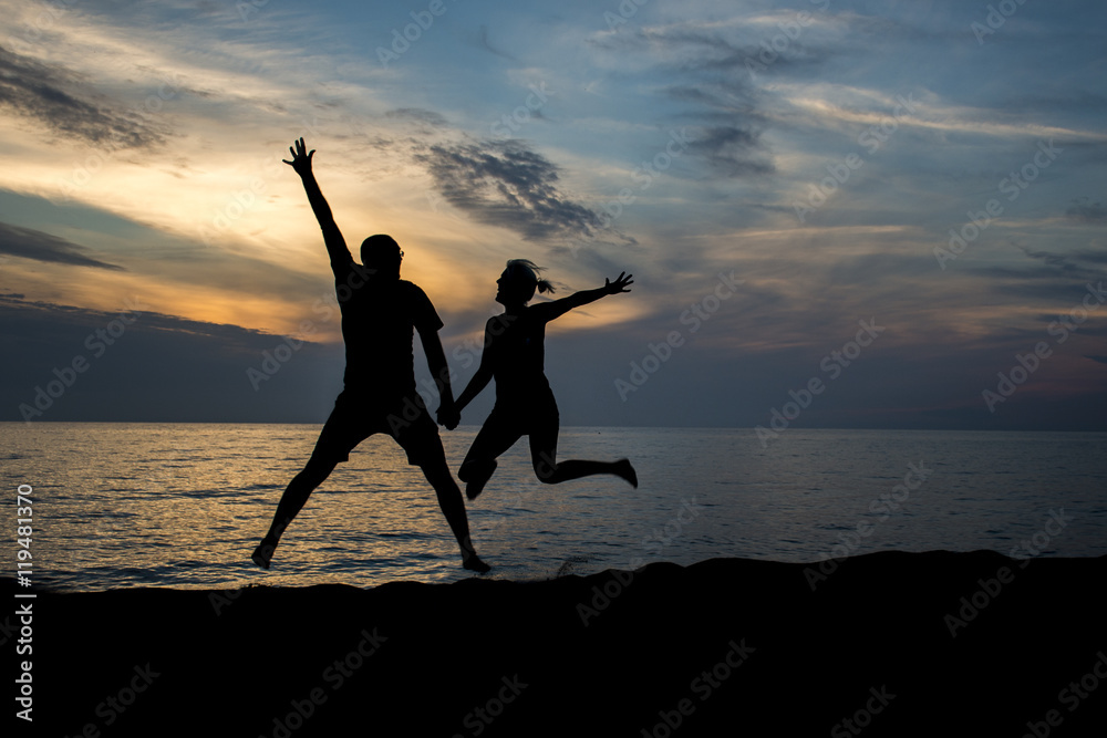 Photo (no illustration) of a couple jump at the beach during sunset