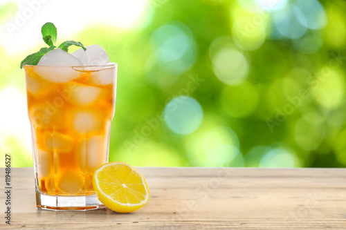 Glass of iced tea on wooden table and blurred green background