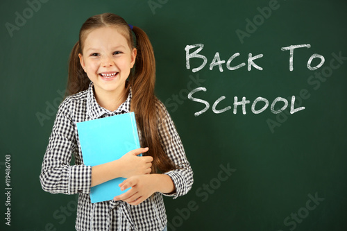 School concept. Cute girl holding book on blackboard background. Text back to school.