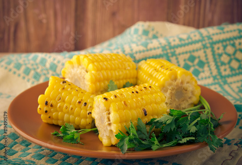 Grilled sweet corn cobs on brown plate with dill
