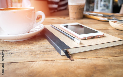 Mobile phone and diary notebook with coffee cup on wood backgrou