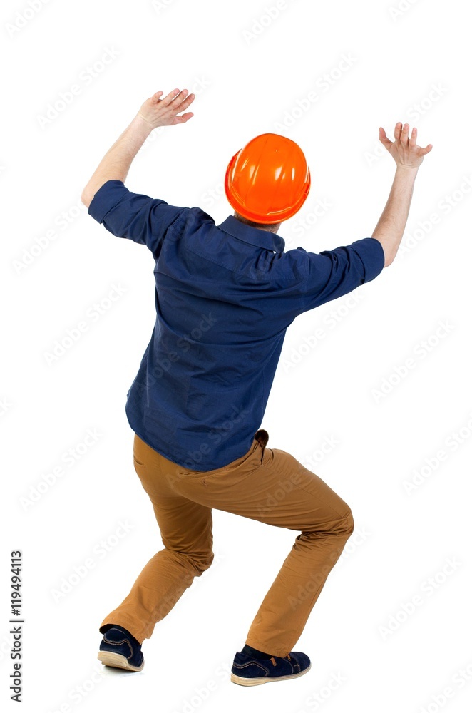 back view business man protective construction helmet protects hands from what is falling from above. engineer in a blue shirt with the sleeves rolled up and a helmet holds out holding a heavy weight back view business man protective construction helmet protects hands from what is falling from above. engineer in a blue shirt with the sleeves rolled up and a helmet holds out holding a heavy weight