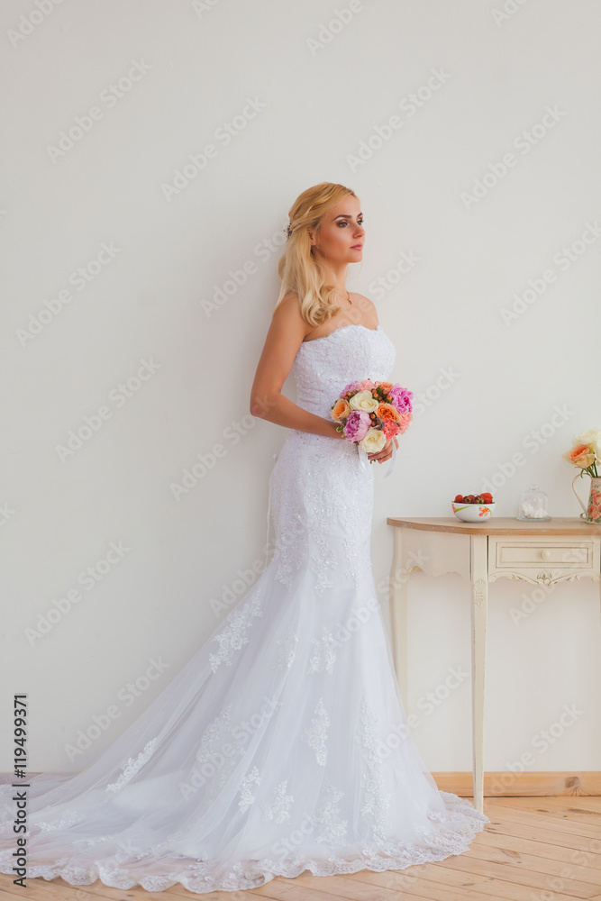 Portrait of a beautiful blonde bride with bouquet in an interior light, wedding concept