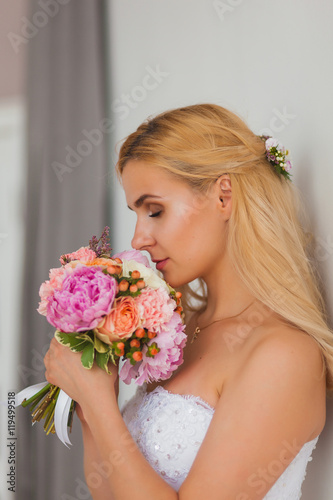 Portrait of a beautiful blonde bride with bouquet in an interior light, wedding concept