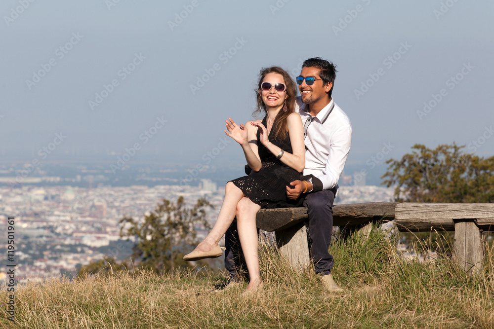 Elegant multiethnic couple sitting on a bench in European countryside