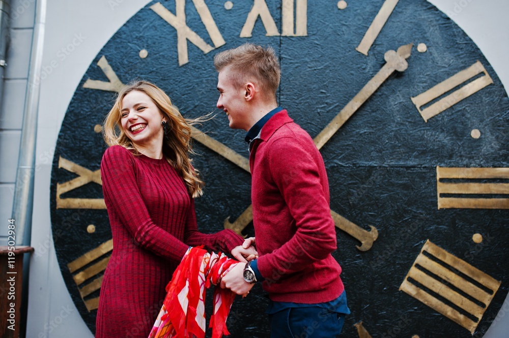 Young beautiful stylish fashion couple in a red dress in love story at the old city, play with shawl background big clock