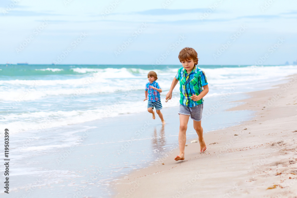 Two little kids boys running on the beach of ocean
