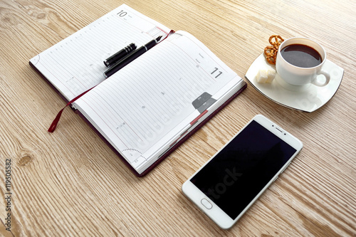 Open notebook, phone with cup of coffee on wooden desk