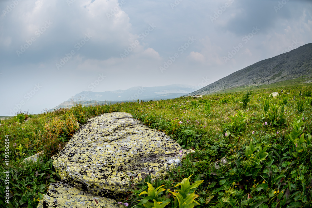 Summer cloudy day in the mountains. Huge stone in the grass. Summer cloudy day in the mountains. Huge stone in the grass.