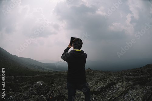 man makes a photo of mountain scenery while standing on top of a mountain in summer photo