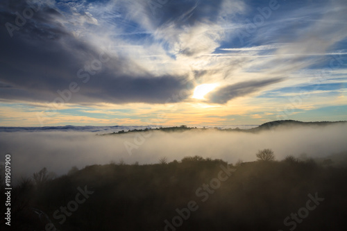 Landscape with the sun setting behind clouds and fog