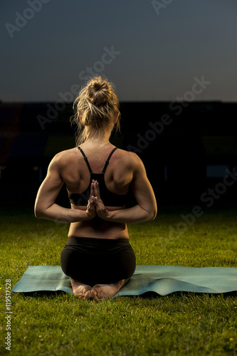 Flexible young woman doing yoga exercises on green grass. Thunderbolt Namaste Pose.