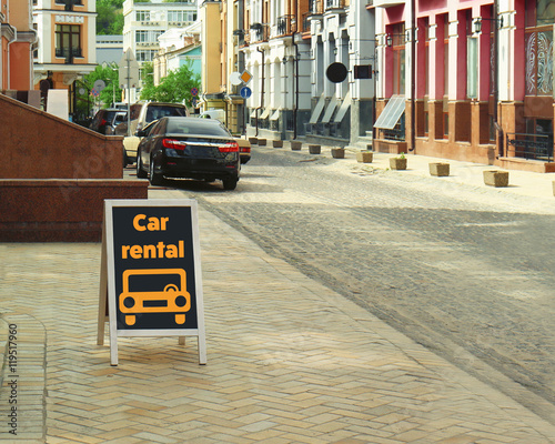 Billboard with text car rental on city street.