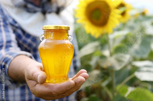 Man holding bottle of honey on sunflower field background