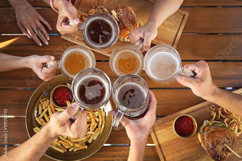 Group of friends drinking beer and eating snacks on wooden background