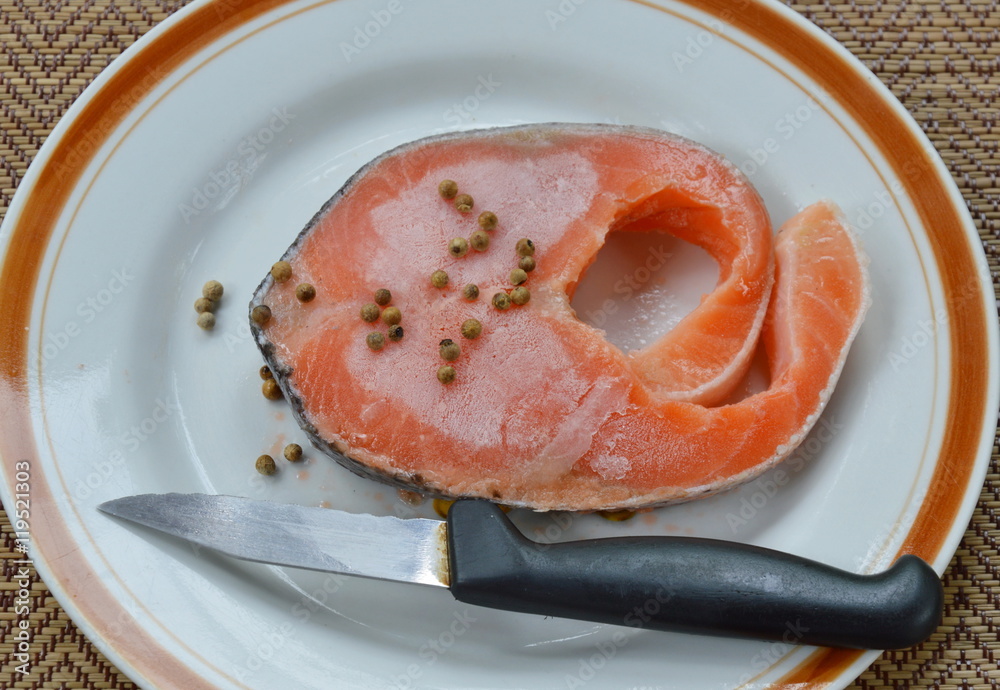 raw frozen salmon dressing pepper and knife on plate