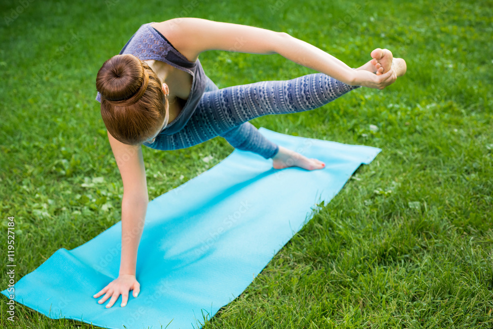 Fototapeta premium Young woman doing yoga exercises in the summer city park.