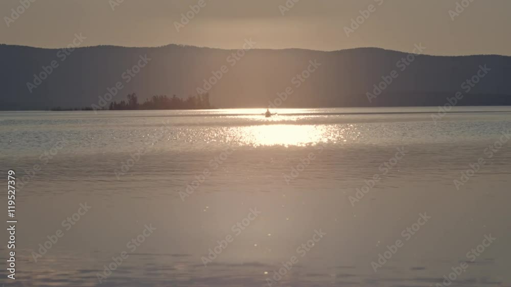 Silhouette of man rowing a kayak on the lake with mountains in the background at sunset Silhouette of man rowing a kayak on the lake with mountains in the background at sunset
