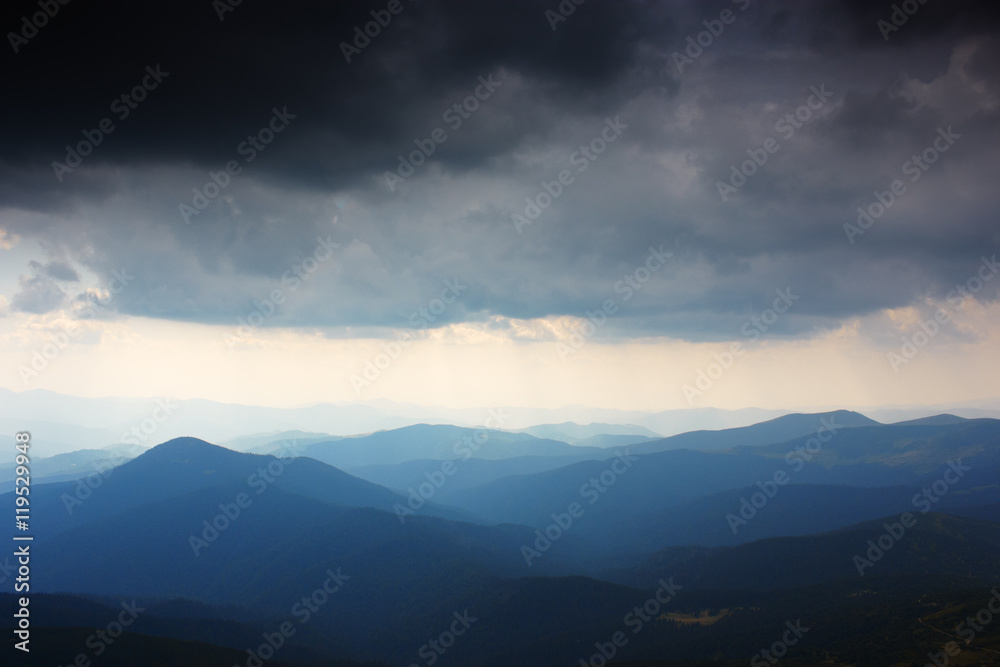 Mountain landscape. Mountain range in haze. Rays of light in lumen of mountains and clouds. Stormy weather. Panorama