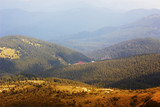 Mountain landscape. Mountain range in haze. Forests on hills, lit by sun. House in mountains. Panorama. Beautiful colors