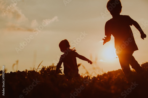 Silhouette of happy boy and girl running at sunset