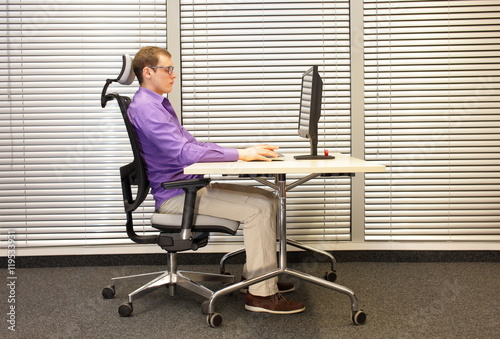 correct sitting position at workstation. man on chair working with pc photo