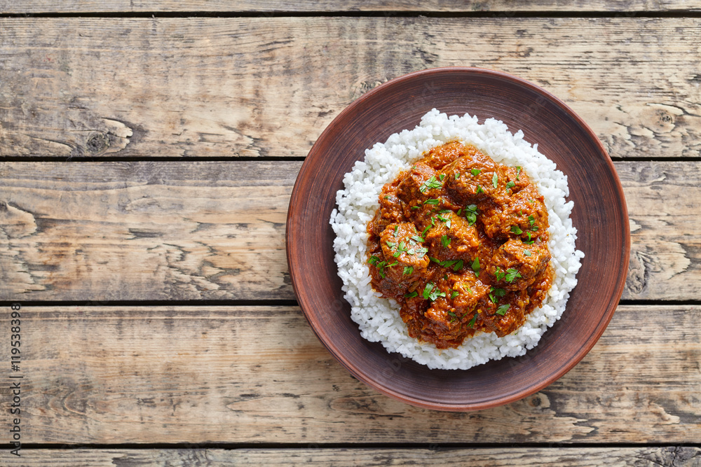 Madras butter Beef spicy slow cook lamb food with rice in clay dish on vintage wooden table background. Delicious India culture restaurant dish. Madras butter Beef spicy slow cook lamb food with rice in clay dish on vintage wooden table background. Delicious India culture restaurant dish.