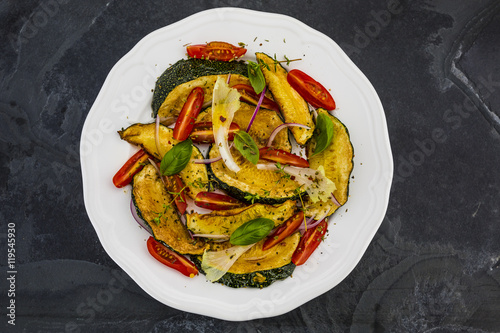 Salad with fried zucchini and tomatoes with herbs served on white plate on stone background . 