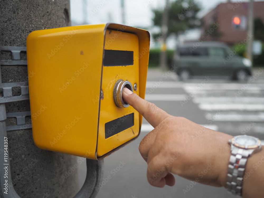 Hand pressing a button at traffic lights on pedestrian crossing.